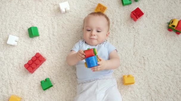 在客厅的地毯上躺着一个笑着的男婴,上面有许多五彩缤纷的玩具.家庭中儿童发展、教育和创造力的概念 — 图库视频影像