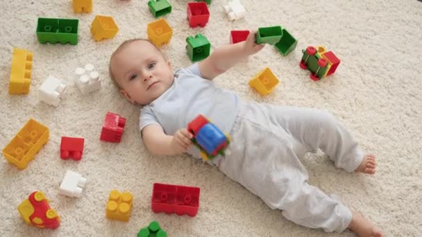 Kleine lachende baby jongen op tapijt in de speelkamer bedekt met kleurrijk speelgoed, bakstenen en blokken. Begrip "ontwikkeling, onderwijs en creativiteit van kinderen thuis" — Stockvideo