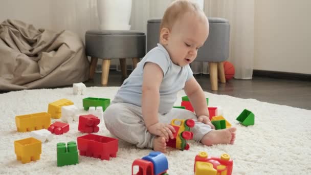 Bébé garçon mignon assis sur le tapis et jouer avec voiture jouet en plastique colroful. Concept de développement, d'éducation et de créativité des enfants à la maison — Video