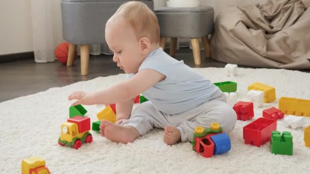 Liten pojke leker på golvet täckt med färgglada leksaker i lekrummet. Begreppet barns utveckling, utbildning och kreativitet i hemmet — Stockvideo