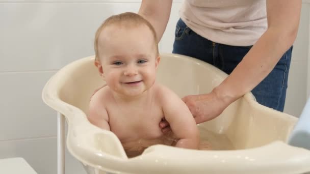 Wesoły uśmiechnięty chłopczyk pluskający wodą i bawiący się podczas kąpieli z matką. Pojęcie higieny dzieci, opieki zdrowotnej i rodzicielstwa. — Wideo stockowe