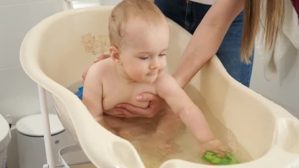 Vidám mosolygós kisfiú játszik játékok és fröccsenő víz műanyag gyermek fürdő. A gyermekhigiénia, az egészségügyi ellátás és a nevelés fogalma. — Stock videók