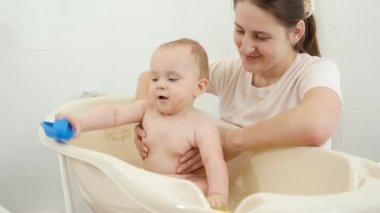 Gülümseyen bir anne kucağında bebeğini evde banyo yaparken seyrediyor. Çocuk hijyeni, sağlık ve ebeveynlik kavramı.