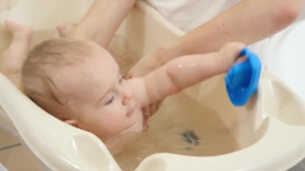 Lindo niño sonriente jugando y nadando en un pequeño baño en casa. Concepto de higiene infantil, atención sanitaria y crianza de los hijos. — Vídeos de Stock