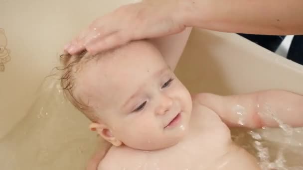 小さなプラスチック製のバスルームでシャンプーで赤ちゃんの息子の頭と髪を洗う母親の閉鎖。子供の衛生、医療、子育ての概念. — ストック動画