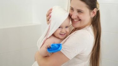 Gülümseyen anne, banyo yaptıktan sonra bebeğini havluyla siliyor. Çocuk hijyeni, sağlık ve ebeveynlik kavramı.