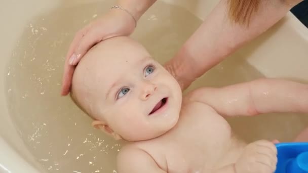 Portret van een lachende schattige kleine jongen die geniet van wassen en zwemmen in bad. Concept van kinderhygiëne, gezondheidszorg en ouderschap. — Stockvideo