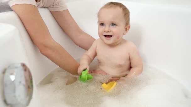 Mère soutenant et tenant son fils bébé assis dans le bain et jouant avec des jouets. Concept d'hygiène, de santé et de développement des enfants à domicile — Video