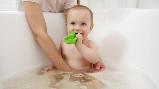 Buon bambino sorridente che gioca con i giocattoli e spruzza acqua nel bagno. Concetto di igiene, assistenza sanitaria e sviluppo dei bambini a casa — Video Stock