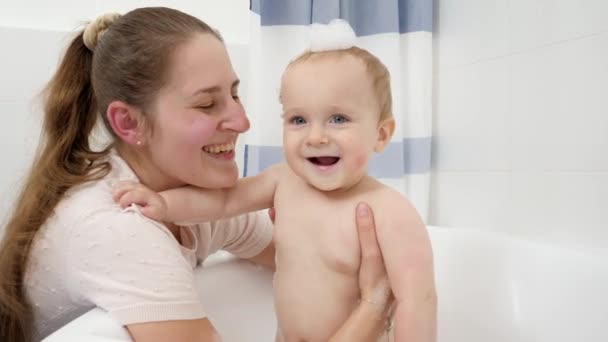 Портрет счастливой улыбающейся матери с маленьким мальчиком, принимающим мыльную ванну. Концепция детской гигиены, здравоохранения и развития на дому — стоковое видео