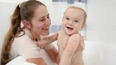 Gülümseyen bebek annesiyle banyoda köpükle yıkanıyor. Evde çocuk hijyeni, sağlık ve geliştirme kavramı