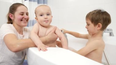 Gülümseyen anne ve büyük oğul, küçük kardeşini banyoda yıkıyorlar. Evde çocuk hijyeni, sağlık ve aile bakımı kavramı