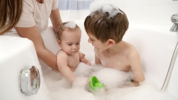 Старший брат грає з дитячим миттям у ванній з піною. Концепція дитячої гігієни, охорони здоров'я та сімейного догляду вдома — стокове відео