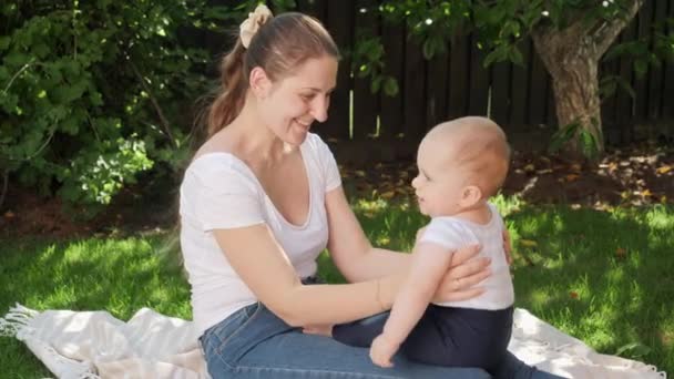 Lykkelig smilende mor som sitter på et teppe i hagen og leker med sin lille sønn. Foreldre, familie, barns utvikling og moro utendørs i naturen. – stockvideo