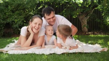 Bebek ve büyük oğlu olan mutlu ebeveynler bahçedeki çimlerde eğleniyor ve dinleniyorlar. Ebeveynlik, aile, çocuk gelişimi ve doğada eğlence..