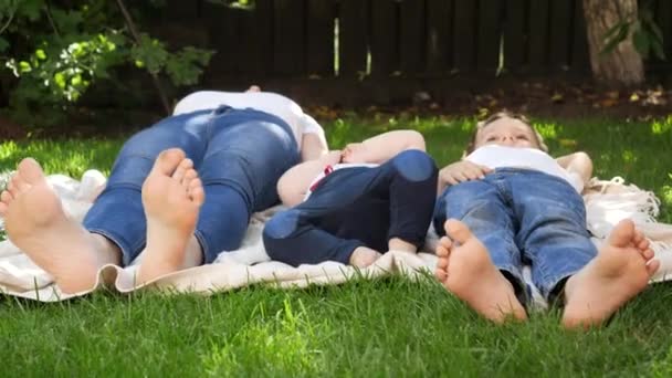 Heureuse famille pieds nus avec des enfants couchés sur l'herbe verte dans le parc. Parentalité, famille, développement des enfants et plaisir en plein air dans la nature. — Video