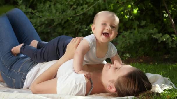 Vrolijk lachend jongetje liggend op moeder in park. Ouderschap, familie, ontwikkeling van kinderen en plezier in de natuur. — Stockvideo