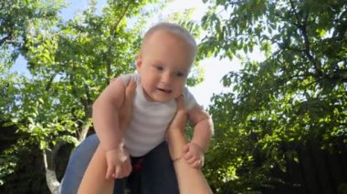 Annenin çimlerin üzerinde yatıp gülümseyen bebeğini parkta kaldırdığı pov. Ebeveynlik, aile, çocuk gelişimi ve doğada eğlence..