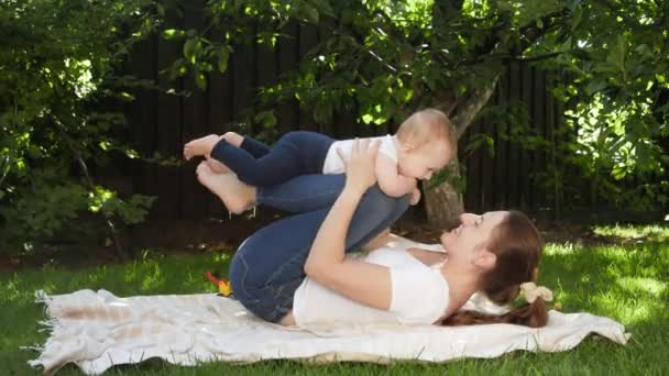 Mère souriante soulevant et berçant son petit fils dans le jardin. Parentalité, famille, développement des enfants et plaisir en plein air dans la nature. — Video