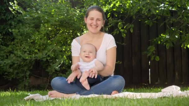 Gelukkig liefhebbende moeder houden en knuffelen haar kleine zoontje terwijl zitten op gras in de tuin. Ouderschap, familie, ontwikkeling van kinderen en plezier in de natuur. — Stockvideo