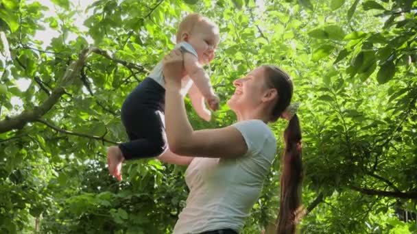 Χαρούμενη χαμογελαστή μητέρα σηκώνεται και κρατάει τον μικρό της γιο σε οπωρώνα με μηλιές. Έννοια των βιολογικών τροφίμων, της διατροφής, της οικογενειακής υγείας και της ανάπτυξης των παιδιών. — Αρχείο Βίντεο