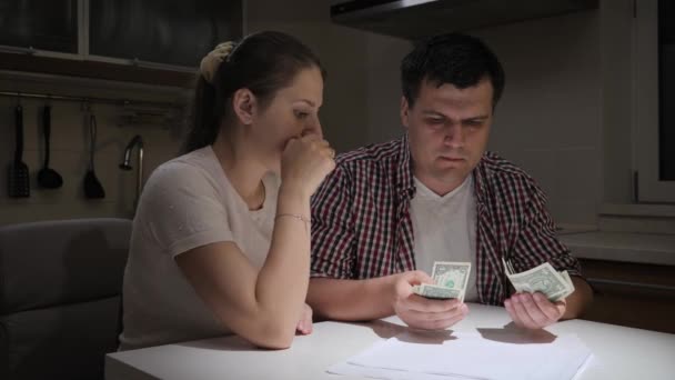 若い男は夜台所に妻と一緒に残されたお金を数える。財政難、貧困、破産、税金、賃貸料の概念. — ストック動画
