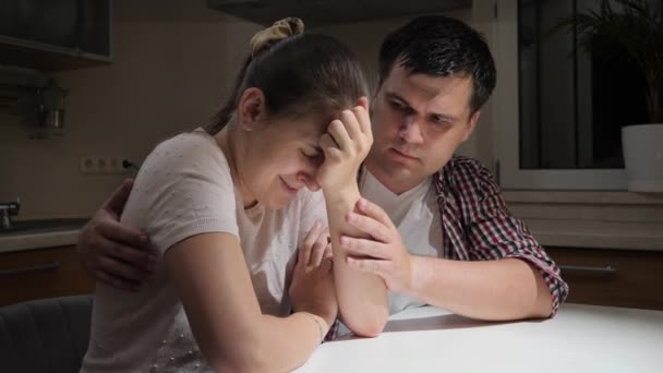 Genç adam geceleri mutfakta ağlayan karısını teselli edip sarılıyor. Umutsuzluk, stres, depresyon, endişe, aile sorunları, boşanma ve hüsran kavramı. — Stok video