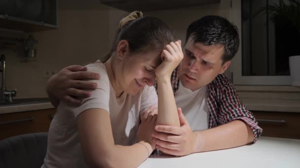 Mujer molesta y estresada llorando y abrazando a su marido en la cocina por la noche. Concepto de desesperación, estrés, depresión, ansiedad, problemas familiares, divorcio y frustración. — Vídeo de stock