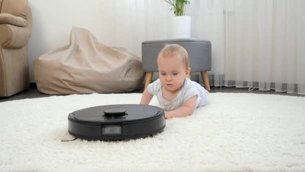 9 mois bébé garçon chassant robot aspirateur plancher aspirateur au salon. Concept d'hygiène, gadgets ménagers et robots à la vie moderne. — Video