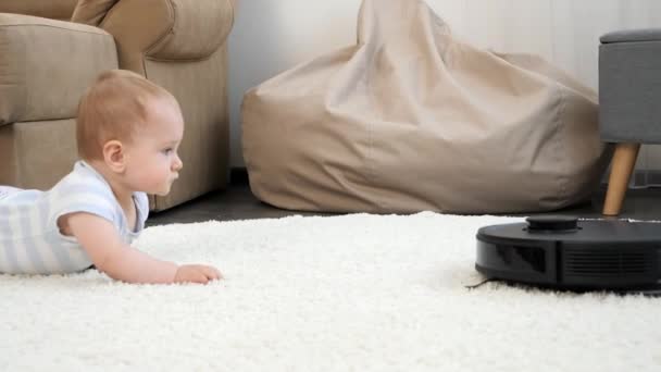 Pequeño niño y robot aspirador acercándose y acercándose a la alfombra en la sala de estar. Concepto de higiene, aparatos domésticos y robots en la vida moderna. — Vídeos de Stock