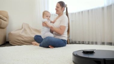 Robot elektrikli süpürge, küçük oğluyla zaman geçirirken kadının ev işlerini yapmasına yardım ediyor. Modern hayatta hijyen, ev aletleri ve robotlar kavramı.