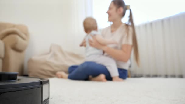 Робот-пилосос працює і робить склепіння, поки мати грає зі своєю дитиною. Концепція гігієни, побутових гаджетів і роботів в сучасному житті . — стокове відео