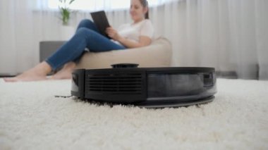 Genç bir kadın oturma odasında çalışırken robot elektrik süpürgesinin kapanışı. Modern hayatta hijyen, ev aletleri ve robotlar kavramı.