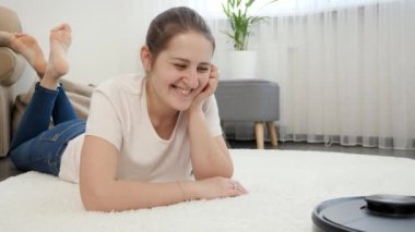 Oturma odasında çalışan yeni robot süpürgesine bakan gülümseyen kadının portresi. Modern hayatta hijyen, ev aletleri ve robotlar kavramı.
