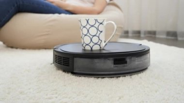 Robot elektrik süpürgesinin ev ofisinde çalışan genç bayana kahve götürmesi. Modern hayatta hijyen, ev aletleri ve robotlar kavramı.