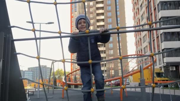 Щасливий усміхнений хлопчик піднімається вгору по мережі на дитячому майданчику. Концепція розвитку дитини, спорту та освіти . — стокове відео