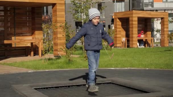 Menino sorridente feliz pulando e jogando no trampolim ao ar livre no playground. Conceito de desenvolvimento infantil, esportes e educação. — Vídeo de Stock