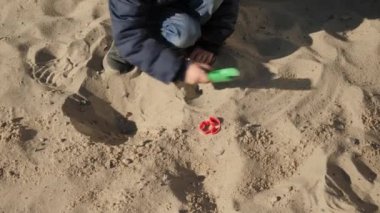 Küçük çocuk kürekle kum kazıyor ve parkta oyun oynuyor. Çocuk gelişimi, spor ve eğitim kavramı.