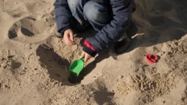 Çocuk bahçesinde plastik kürekle kum kazıyor. Çocuk gelişimi, spor ve eğitim kavramı.