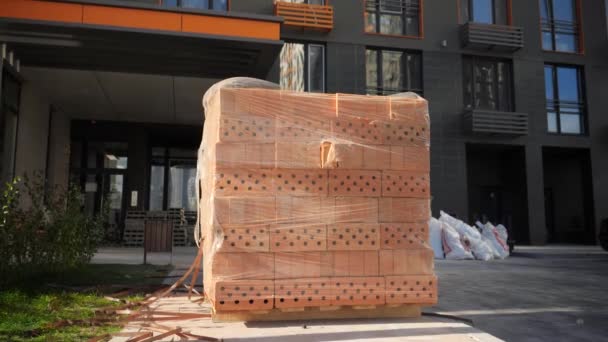 Grande pilha ou tijolos de construção vermelho em paletes de madeira no local de construção — Vídeo de Stock
