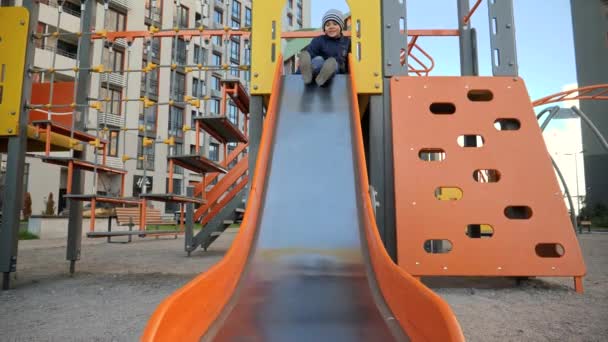 Szczęśliwy wesoły chłopiec jeżdżący na zjeżdżalni na placu zabaw i uśmiechnięty przed kamerą. Koncepcja rozwoju dzieci, sportu i edukacji. — Wideo stockowe
