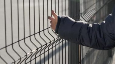 Küçük bir çocuğun metal çitin yanından geçerken eliyle ona dokunduğu yakın plan. Yoksulluk, göç, zorbalık ve çocuklar stresi