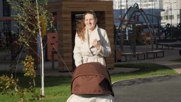 Retrato de mulher sorridente com bebê em carrinho ou carrinho andando no parque no dia ventoso. Conceito de desenvolvimento infantil, parentalidade e cuidado familiar. — Vídeo de Stock