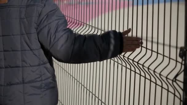 Primo piano di ragazzo toccando recinzione rete metallica e camminando passato. Concetto di povertà, immigrazione, bullismo e stress infantile — Video Stock