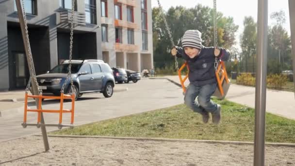 Feliz sorrindo e rindo menino balançando no parque infantil no novo pátio. Conceito de desenvolvimento infantil, esportes e educação. — Vídeo de Stock