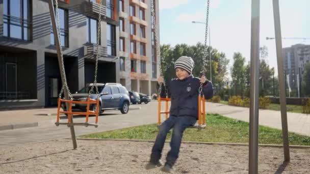 Улыбающийся мальчик качается на качелях на детской площадке. Концепция развития ребенка, спорта и образования. — стоковое видео