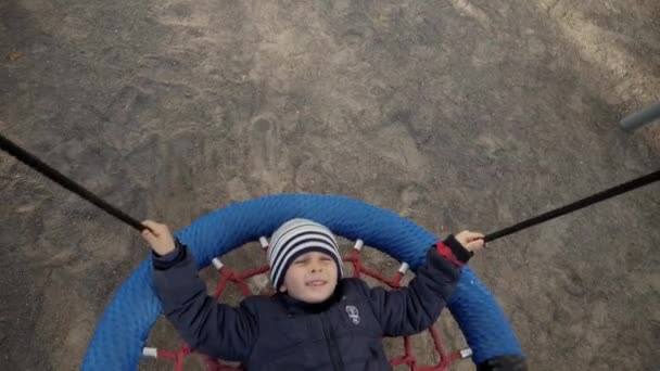 Muchacho sonriente acostado y divirtiéndose en el columpio de cuerda en el palyground chidlren en el parque. Concepto de desarrollo infantil, deportes y educación. — Vídeos de Stock