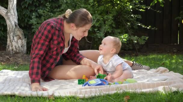 Sonriente joven madre jugando con su pequeño hijo en la manta en el parque. Concepto de desarrollo infantil, pasar tiempo en familia y crianza de los hijos. — Vídeo de stock