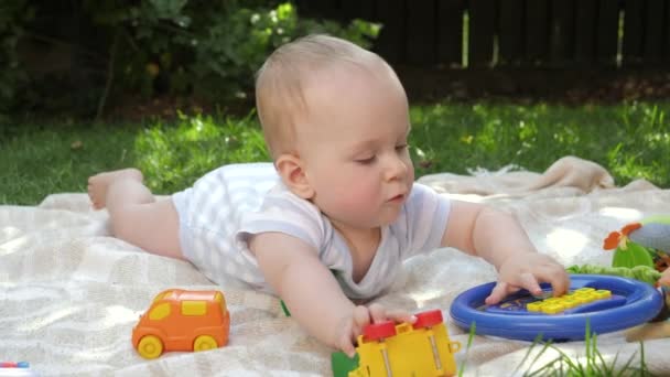 Bebê bonito rastejando na grama para brinquedos coloridos. Conceito de desenvolvimento precoce da criança, educação e relaxamento ao ar livre. — Vídeo de Stock