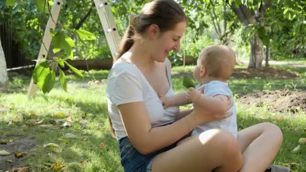 Portret van een lachende jonge vrouw met een zoontje dat naar bomen in de tuin kijkt. Concept van de ontwikkeling van het kind, familie die samen tijd doorbrengt en ouderschap. — Stockvideo